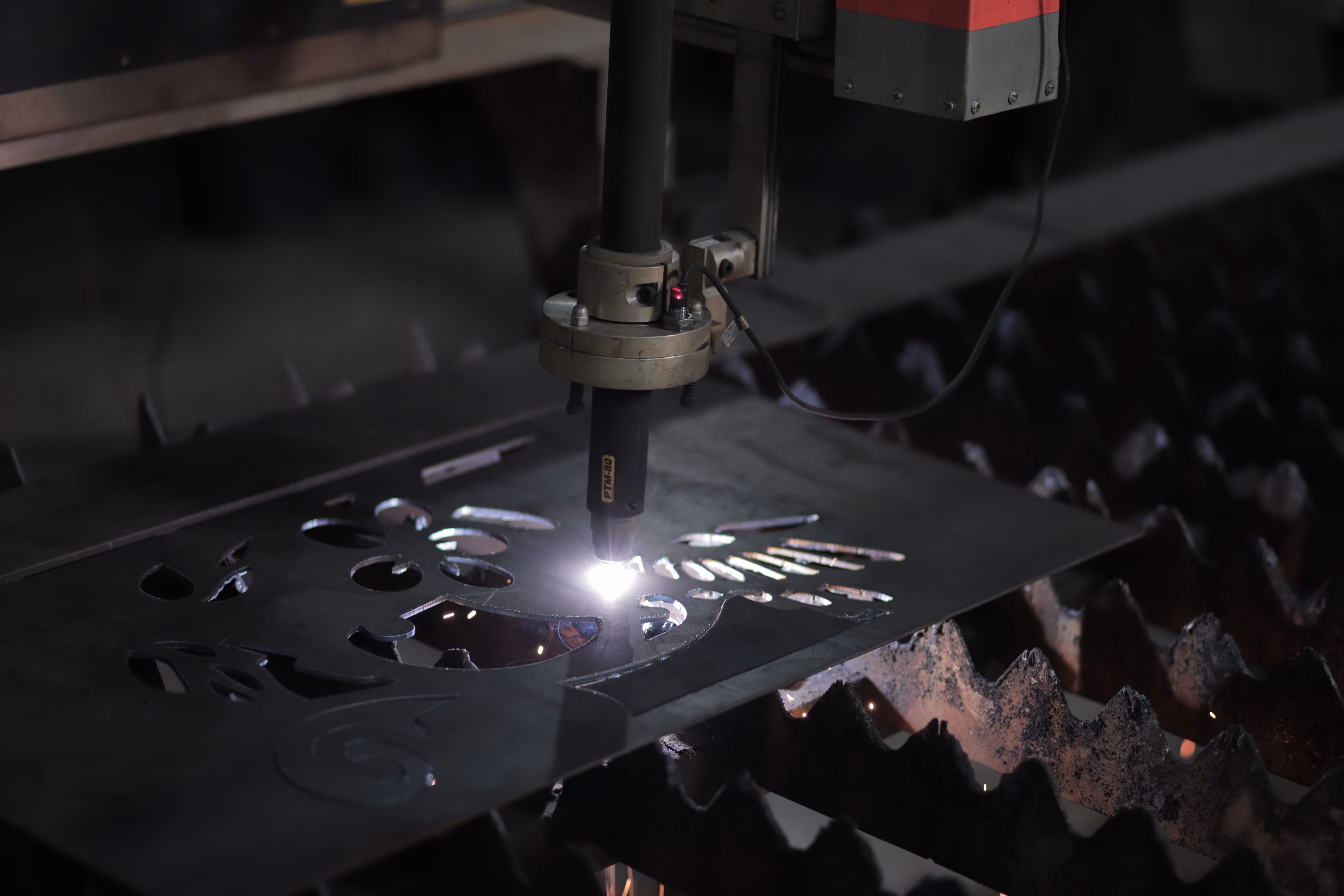 Primo piano della torcia plasma PTM-80 durante il taglio CNC di una lamiera — getto arancione e alone luminoso della camera di combustione